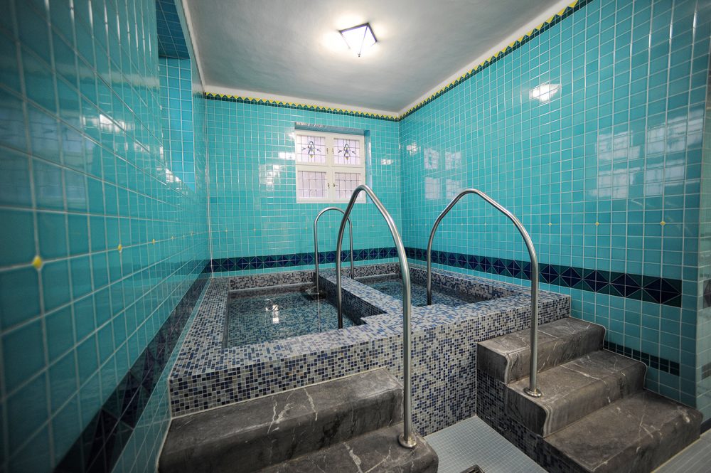 Tre scalini di marmo grigio portano al percorso Kneipp e alle antiche finestre di vetro Tiffany.