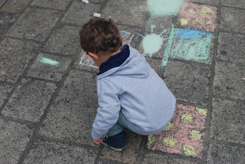 Kind malt mit Kreide am Boden vor der Bücherei Telfs