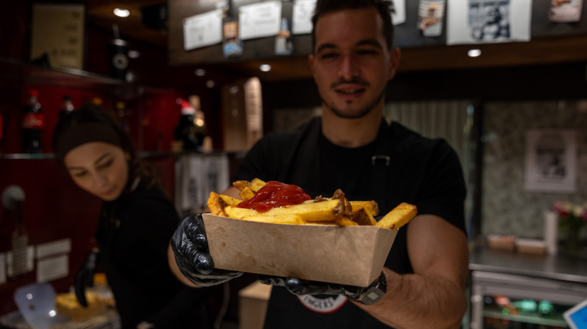 Mann reicht Pommes über die Theke.
